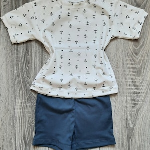 May include: A white short-sleeved shirt with a pattern of small anchors and hearts. The shirt is paired with dark blue shorts.