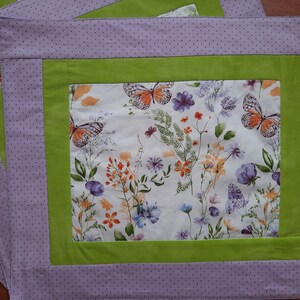 May include: A purple and green placemat with a white background featuring a floral pattern with butterflies. The placemat has a dotted pattern around the border.