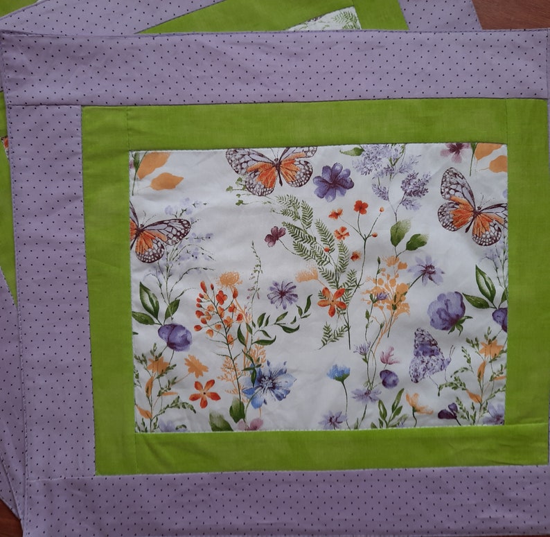 May include: A purple and green placemat with a white background featuring a floral pattern with butterflies. The placemat has a dotted pattern around the border.