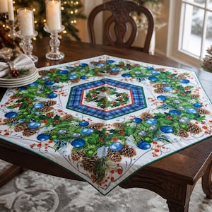 Peut inclure: Un chemin de table carré en tissu orné d'un hexagone central avec une bordure à carreaux bleus et du houx. L'imprimé présente une couronne de branches de pin vertes, de pommes de pin brunes, de baies rouges et de boules de Noël bleues.