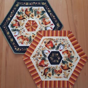 Può includere: Due tovaglie esagonali con un designo di gallo e girasole. La tovaglia in alto è nera con accenti bianchi e gialli. La tovaglia in basso è bianca con accenti arancioni, rossi e gialli.