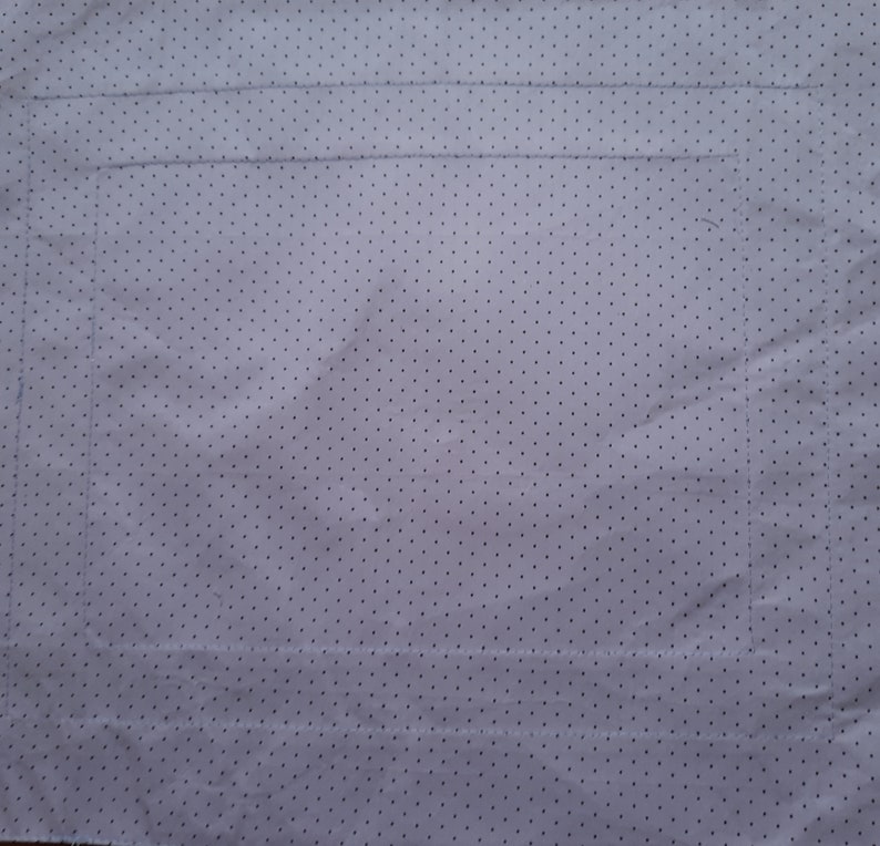 May include: A white fabric with a small black polka dot pattern. The fabric has been marked with lines to indicate where to sew.