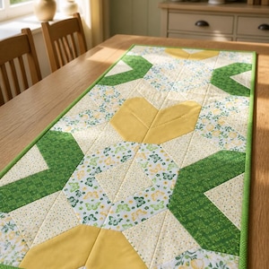 May include: A rectangular quilted table runner featuring a patchwork design of yellow, white, and green fabric. The pattern includes solid yellow leaf-like shapes, green geometric sections, and white fabric printed with small yellow flowers and green butterflies.