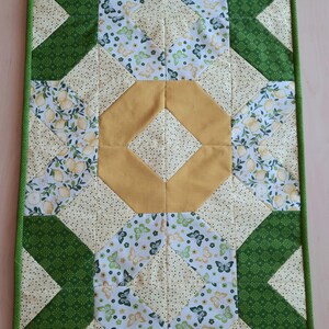 May include: A rectangular quilted table runner featuring a patchwork design with green, yellow, and white fabric. The pattern includes sections with lemon prints, butterfly motifs, and solid mustard yellow diamonds, all bordered by a green trim.
