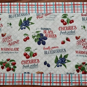 Könnte beinhalten: Ein weißer Stofftischset mit einem rot-weiß-blauen karierten Rand. Die Mitte des Tischsets zeigt ein sich wiederholendes Muster aus Blaubeeren, Kirschen und Brombeeren mit dem Text "Rise and Shine Marmalade with Locally Grown Fruit", "Summer Black Berries", "Locally Grown Blueberries", "Cherries Fresh Picked", und "Fresh Homemade Pies Cakes Pastries".