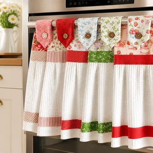 Peut inclure: Cinq torchons de cuisine suspendus avec un tissu blanc gaufré et des hauts en tissu à motifs dans des tons rose, rouge, bleu et vert. Chaque torchon comporte une patte en tissu avec un bouton en bois pour le fixer à une poignée de four.