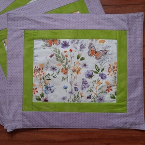 May include: A purple and green fabric placemat with a white background featuring a floral pattern with butterflies.