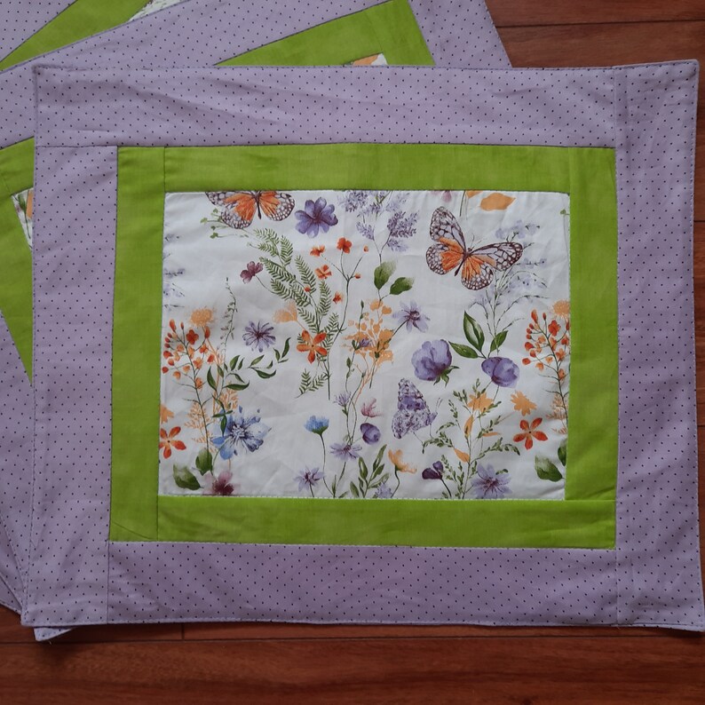 May include: A purple and green fabric placemat with a white background featuring a floral pattern with butterflies.