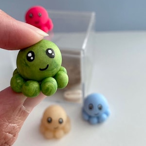 May include: A set of four small octopus figurines. The octopus are made of green, blue, pink and beige clay. Each octopus has a cute face with eyes and a smile.