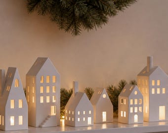 Może przedstawiać: Sześć białych ceramicznych modeli domów z wyciętymi oknami i drzwiami, oświetlonych od wewnątrz. Tekst CHRISTMAS HOUSES - SIX HOUSE MODEL 3D STL FILES jest widoczny u góry. Te konstrukcje charakteryzują się zróżnicowanymi projektami.