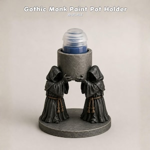 May include: A gray paint pot holder featuring two hooded figures in robes with rope belts, standing on a circular base and supporting a central cylindrical container. A blue paint pot with a clear lid is inserted into the holder. Text reads: Gothic Monk Paint Pot Holder 3D STL FILE.