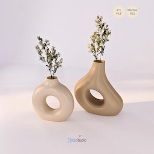 K&ouml;nnte beinhalten: Zwei beige Keramikvasen mit einzigartigen, offenen Kreisdesigns. Jede Vase enth&auml;lt eine kleine Anordnung getrockneter Blumen. Die Vasen stehen vor einem wei&szlig;en Hintergrund und schaffen eine minimalistische &Auml;sthetik.
