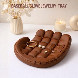 May include: A brown baseball glove-shaped jewelry tray with a stitched design. The tray holds a gold bracelet, pearl earrings, and two necklaces. The text "BASEBALL GLOVE JEWELRY TRAY" is visible.