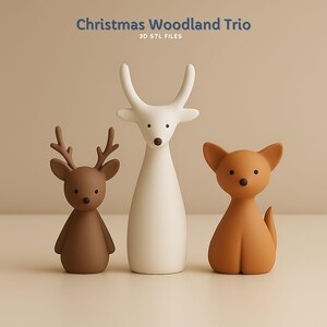 May include: Three minimalist Christmas figurines: a brown deer, a white deer, and a tan fox. The text "Christmas Woodland Trio" and "3D STL FILES" are at the top. The figurines have simple, rounded shapes and are set against a neutral background.