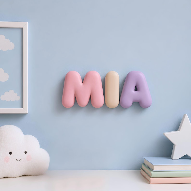 May include: A wall-mounted decorative sign spelling the name MIA in three-dimensional, rounded, bubble-style letters. The letter M is pink, the letter I is cream, and the letter A is light purple, all featuring a smooth, matte finish.