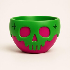 May include: A round bowl featuring a bright green skull overlay with a dripping effect over a solid magenta base. The green skull design includes two star-shaped cutouts on the sides and hollowed-out eye sockets that reveal the magenta color underneath.