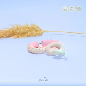 May include: Two pink and white donut-shaped 3D printed earrings with a white background. The earrings are made of a smooth, glossy material and have a subtle ombre effect. The earrings are perfect for adding a touch of whimsy to any outfit.