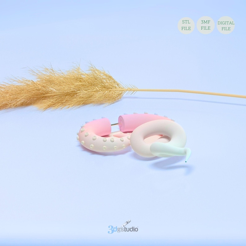 May include: Two pink and white donut-shaped 3D printed earrings with a white background. The earrings are made of a smooth, glossy material and have a subtle ombre effect. The earrings are perfect for adding a touch of whimsy to any outfit.