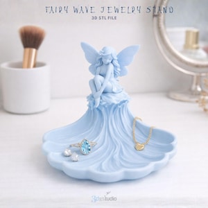 Puede incluir: Un joyero de onda de hadas azul claro con una figura de hada. El soporte contiene un collar de corazón dorado y un anillo con una piedra preciosa azul. El texto "FAIRY WAVE JEWELRY STAND" y "3D STL FILE" son visibles.