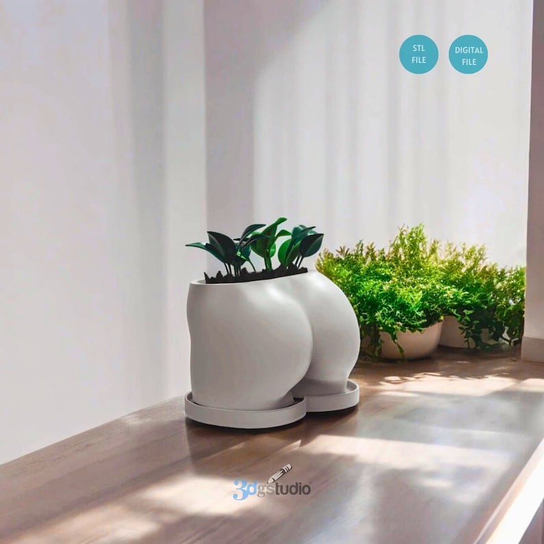 May include: A white ceramic planter shaped like a pair of buttocks, holding green plants. The planter sits on a matching saucer. The image also shows other potted plants in the background. The text "STL FILE" and "DIGITAL FILE" are visible.