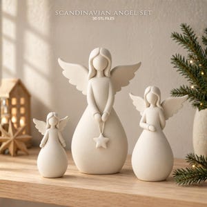 Könnte beinhalten: Ein Set aus drei cremeweißen Engelfiguren mit glatten, abgerundeten Formen und ausgebreiteten Flügeln. Der mittlere Engel hält einen kleinen Stern. Der Text SCANDINAVIAN ANGEL SET 3D STL FILES ist oben im Bild zu sehen.