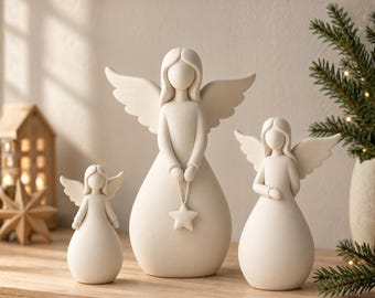 May include: A set of three off-white angel figurines with smooth, rounded forms and outstretched wings. The central angel holds a small star ornament. The text SCANDINAVIAN ANGEL SET 3D STL FILES is visible at the top of the image.