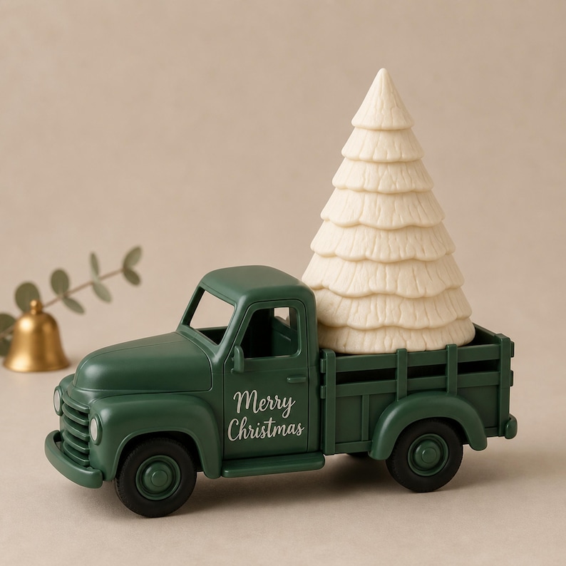 Op de afbeelding: Een donkergroene speelgoedpickup met de tekst Merry Christmas op de deur. De laadbak van de truck vervoert een grote, getextureerde, gebroken witte kegelvormige kerstboomfiguur. Het voertuig heeft een klassiek ontwerp met ronde koplampen.