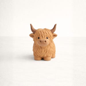 May include: A small, tan-colored Highland cow figurine. The toy cow has a shaggy coat, small brown horns, and a cute, friendly expression. The figurine is made of a soft material and is suitable for children.