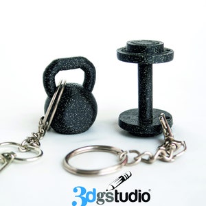 Może przedstawiać: Czarno-srebrny brelok z miniaturowym urokiem kettlebell i hantle. Urok jest wykonany z materiału w kropki i ma wygląd druku 3D. Brelok jest przymocowany do srebrnego łańcuszka i kółka. Obraz zawiera również tekst "3dgstudio".