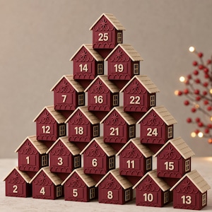 May include: A pyramid-shaped advent calendar composed of twenty-five individual maroon house-shaped boxes with beige roofs. Each house features a unique number from 1 to 25 printed on the front, along with a star motif and small window details.