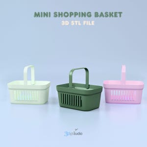 May include: Three miniature shopping baskets in pastel colors: light green, dark green, and pink. Each basket has a handle and a rectangular shape with vertical slats. Text at the top reads "MINI SHOPPING BASKET 3D STL FILE".