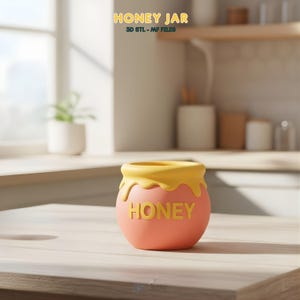 May include: A round, matte-finish honey jar featuring a coral-pink base and a yellow rim with a dripping honey design. The word HONEY is embossed in yellow on the front. The text HONEY JAR 3D STL - MF FILES appears at the top of the image.
