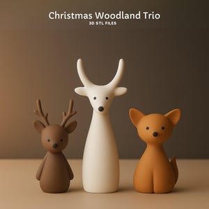 May include: A trio of woodland animal figurines. The set includes a brown deer with antlers, a tall white deer, and a tan fox. The text "Christmas Woodland Trio" and "3D STL FILES" are at the top.