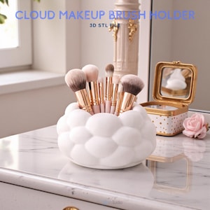 Könnte beinhalten: Ein weißer, wolkenförmiger Make-up-Pinselhalter, gefüllt mit Make-up-Pinseln. Der Halter steht auf einer Marmoroberfläche. Der Text lautet "CLOUD MAKEUP BRUSH HOLDER" und "3D STL FILE". Eine kleine gold-weiße Box und eine rosa Rose befinden sich im Hintergrund.