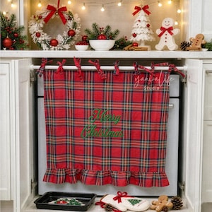 May include: A red, green, and blue tartan oven handle cover with a ruffled bottom edge and the embroidered green text Merry Christmas. The fabric cover hangs from a white rod and features fabric ties at the top for secure attachment.