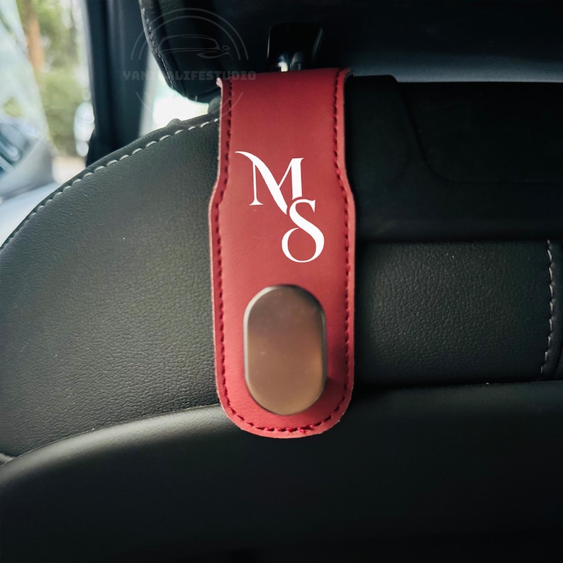 Peut inclure: Un crochet de voiture en cuir bordeaux pour appui-t&ecirc;te, avec les initiales blanches "MS". Le crochet est dot&eacute; d'un bouton ovale m&eacute;tallique et est con&ccedil;u pour se fixer &agrave; un appui-t&ecirc;te de voiture. Les bords sont cousus.