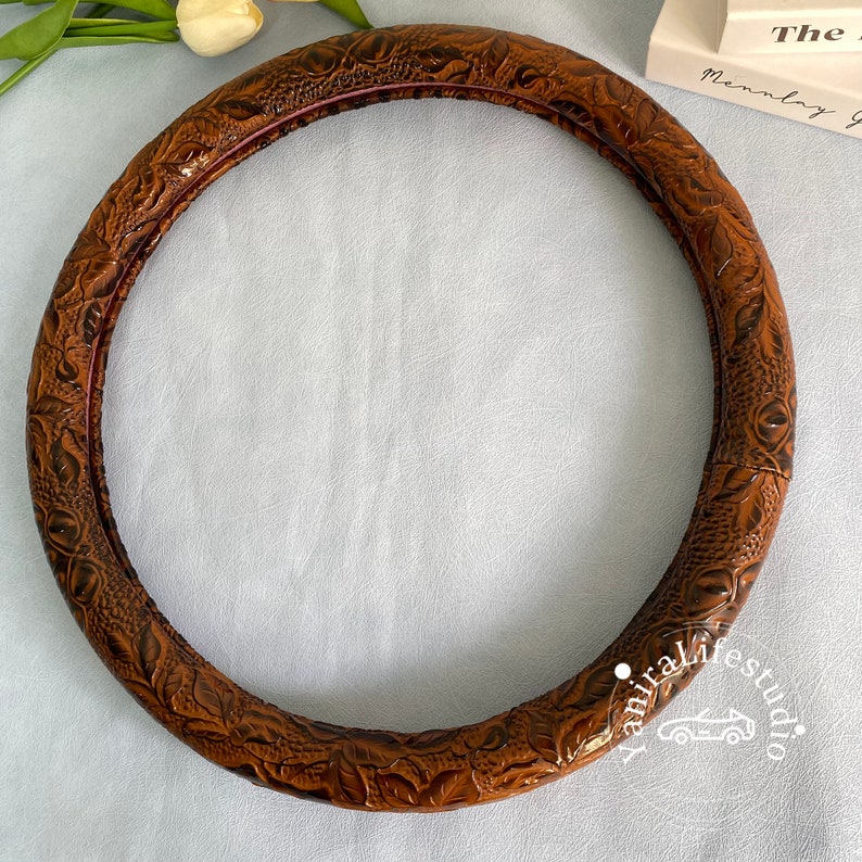 Peut inclure: Housse de volant en cuir marron avec un motif floral en relief.