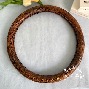 Peut inclure: Housse de volant en cuir marron avec un motif en relief floral et le mot "CUSTOM" en lettres dor&eacute;es.