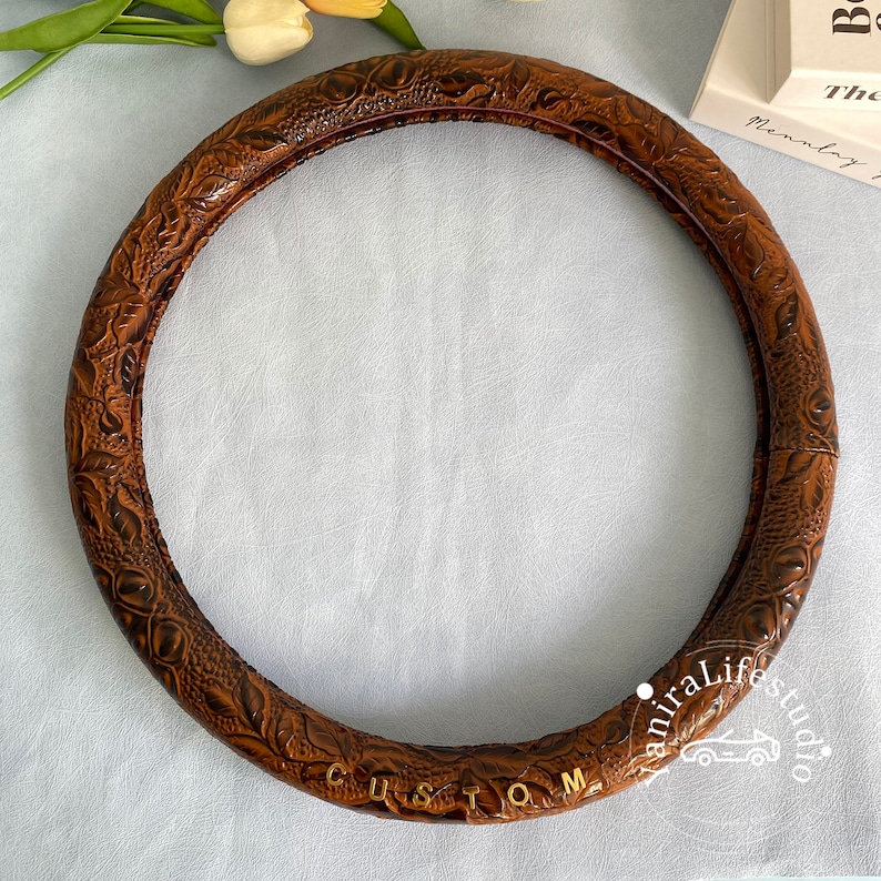 Peut inclure: Housse de volant en cuir marron avec un motif en relief floral et le mot "CUSTOM" en lettres dor&eacute;es.