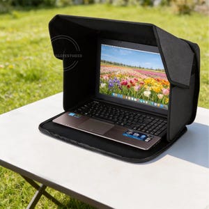 May include: A black laptop sun shade hood attached to a laptop computer. The screen displays a colorful field of tulips. The hood features side panels and a top flap to reduce glare on the screen. The laptop has a black keyboard and trackpad.