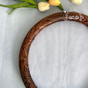 Peut inclure: Un couvre-volant en cuir marron avec un motif floral en relief. Le couvre-volant est sur une surface textur&eacute;e blanche.