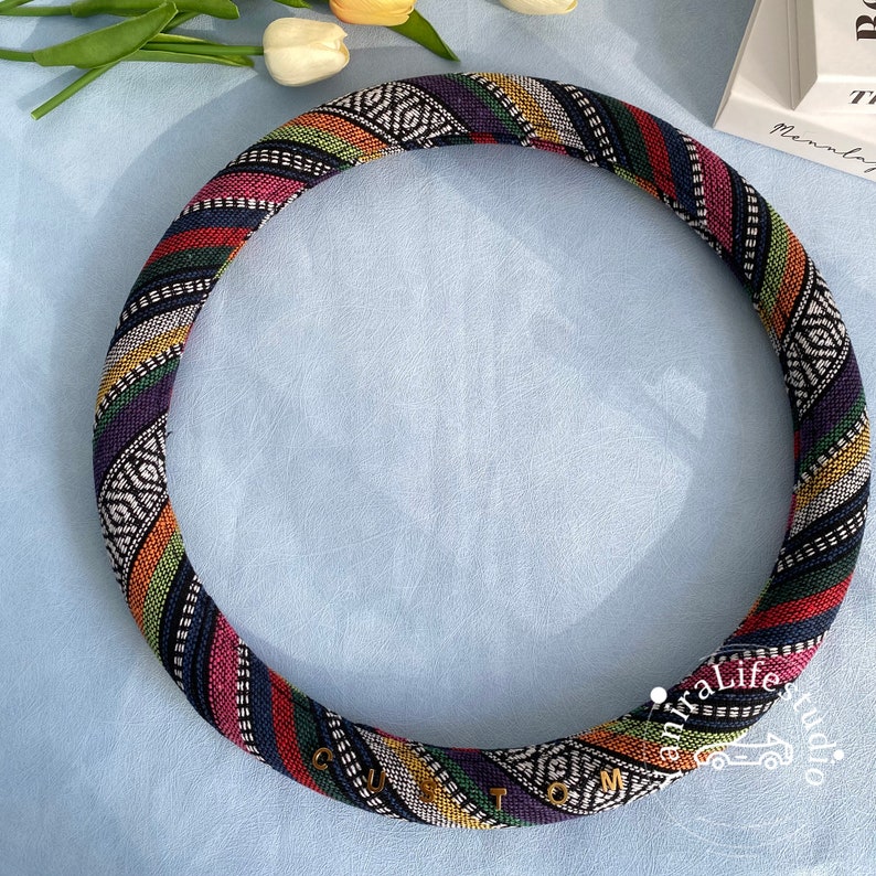 May include: A colorful patterned steering wheel cover with black, white, red, yellow, green, and purple stripes. The cover has the word "CUSTOM" written in gold letters.