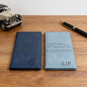 May include: Two leather registration and insurance holders in navy blue and light blue. Each features a car silhouette and the text "REGISTRATION & INSURANCE". One has initials "ABC", the other "L|F".