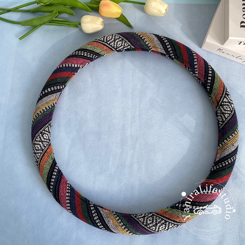 May include: A colorful patterned steering wheel cover with black, red, green, yellow, and white stripes. The cover is made of fabric and has a geometric design.