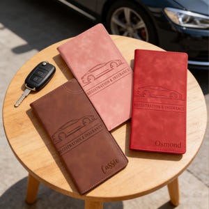 May include: A collection of car registration and insurance holders in various colors: brown, pink, and red. Each holder features a car silhouette and the text "REGISTRATION & INSURANCE". One holder is personalized with the name "Cassie", and another with "Osmond".