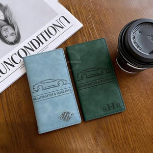 May include: Two leather registration and insurance holders. One is light blue, the other is dark green. Each has a car graphic and the words "REGISTRATION & INSURANCE". The light blue one has "ABC" in a diamond shape.