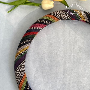 May include: A colorful patterned steering wheel cover with black, white, red, green, yellow, and blue stripes. The cover is made of fabric and has a woven design.