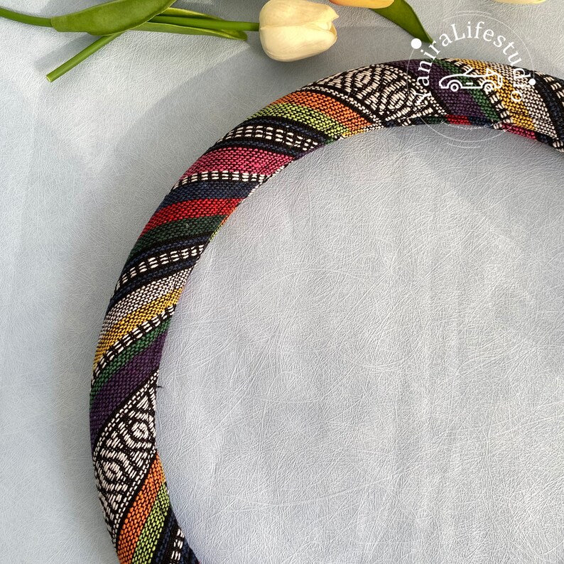 May include: A colorful patterned steering wheel cover with black, white, red, green, yellow, and blue stripes. The cover is made of fabric and has a woven design.