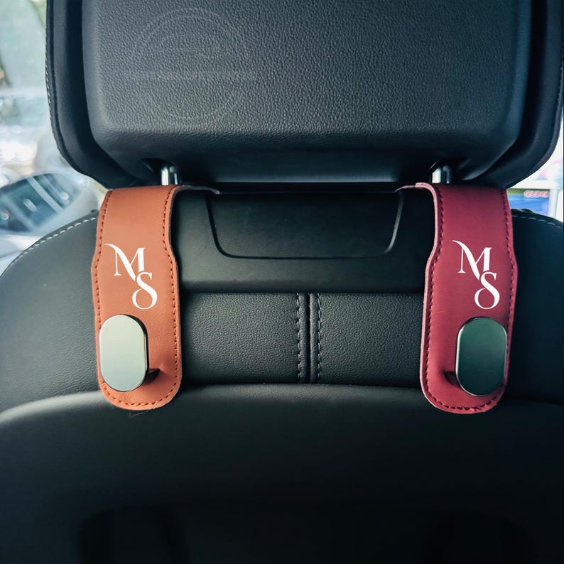Peut inclure: Deux crochets d'appui-t&ecirc;te de voiture, l'un brun rouge&acirc;tre et l'autre bordeaux. Chaque crochet porte les lettres blanches "MS". Les crochets ont une base magn&eacute;tique argent&eacute;e.