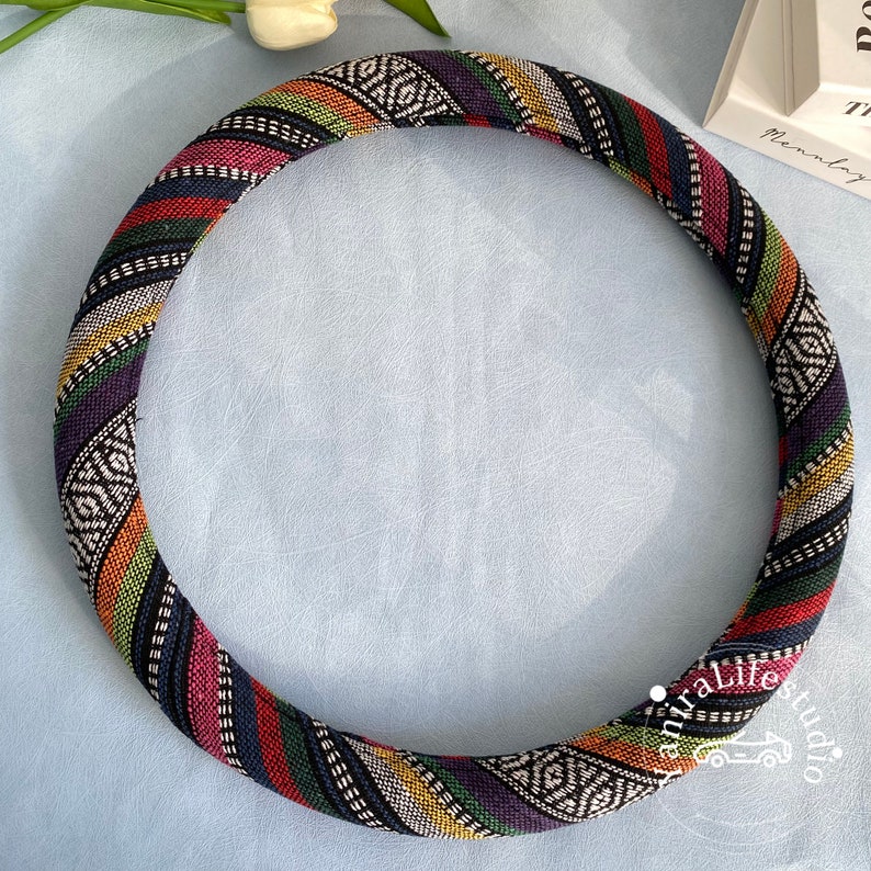 May include: A colorful, patterned steering wheel cover with a black background and stripes of red, yellow, green, and blue. The cover is made of fabric and has a geometric design.